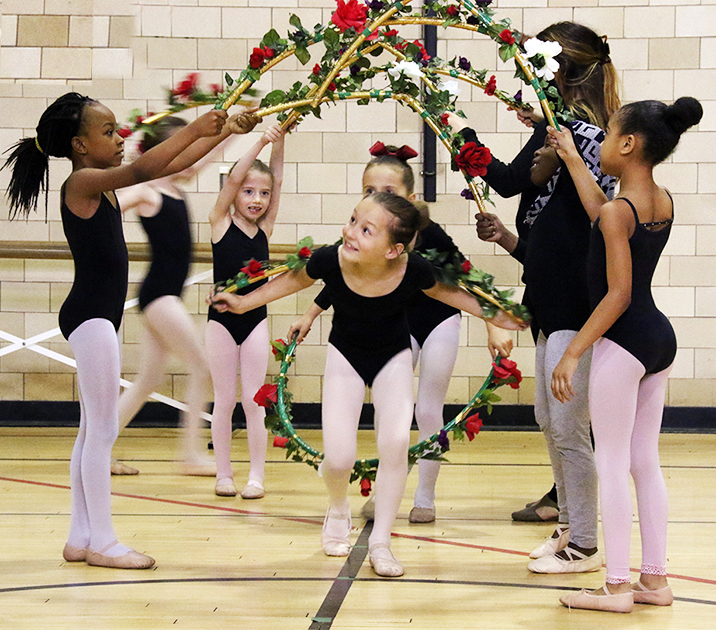 Young dancers in black leotards and pink tights forming a tunnels with flowers and a little girl running through